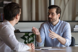 Confident advisor Real Estate Agent broker manager in glasses consulting client about contract terms at meeting in office, sitting at table, two business partners negotiating, mentor teaching new employee
