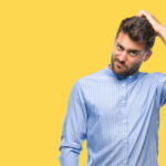 Young handsome man over isolated background confuse and wonder about question. Uncertain with doubt, thinking with hand on head. Pensive concept.